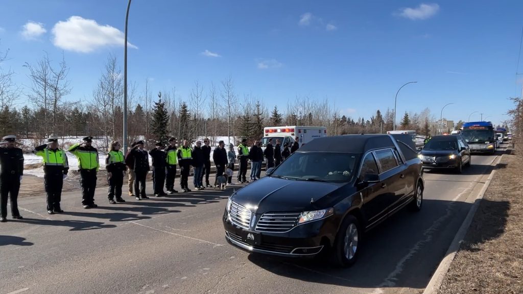 black hearses drive by saluting officers