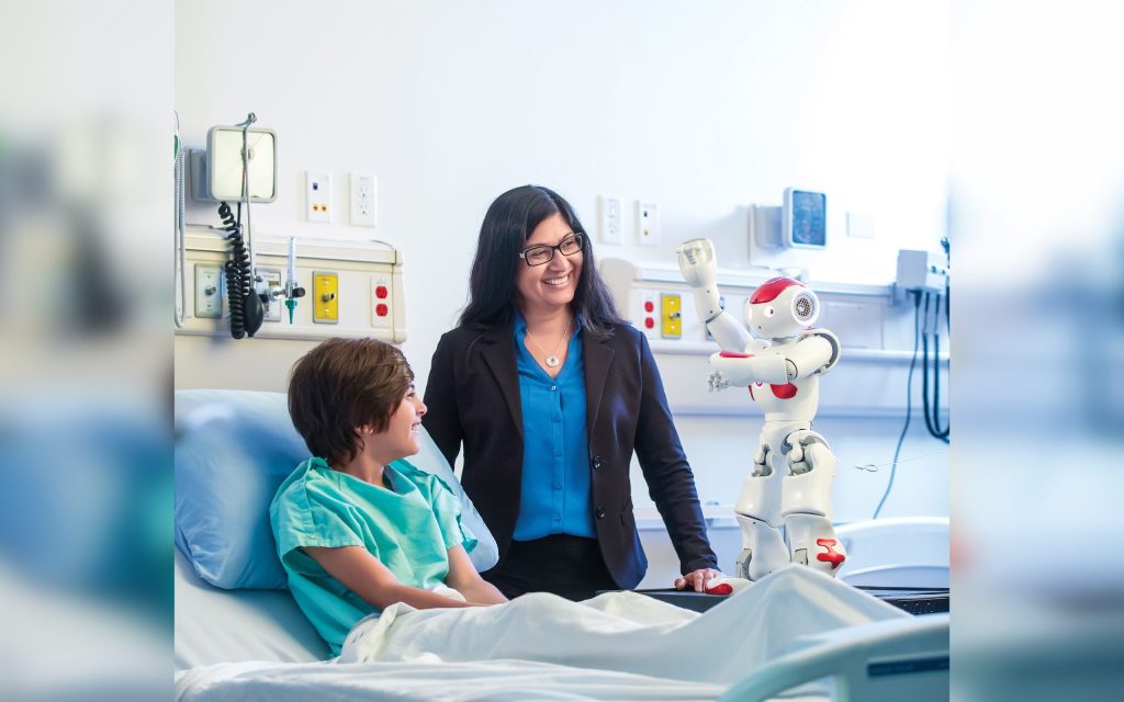 child in hospital bed, adult by his side, with robot